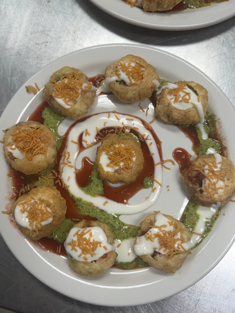 Dahi puri topped with yogurt, tamarind chutney, green chutney, and crispy sev on a white plate.